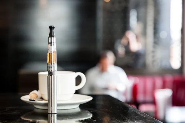 Электронная сигарета на барной стойке с чашкой кофе — стоковое фото