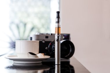 E-cigarette on a bar with coffee and a camera clipart