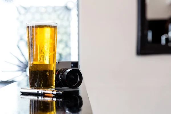 E-cigarette lying alongside beer and a camera — Stock Photo, Image