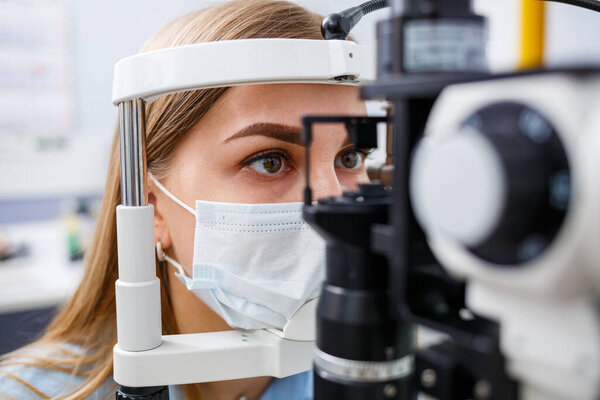 Young woman sitting in armchair looking at slit lamp during medical examination in eyes