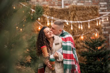 Beyaz elbiseli güzel genç bir çift bahçede bir Noel ağacının yanında oturuyorlar. Mutlu erkek ve kadın, romantizm, Noel kutlaması, eğlence, aşk.