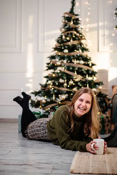金发漂亮的年轻女子坐在圣诞树边喝咖啡 新年快到了 一个舒适的家的圣诞气氛 — 图库照片