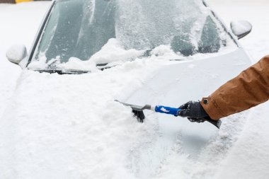 Genç bir adam arabasındaki karı temizler. Kışın araba bakımı