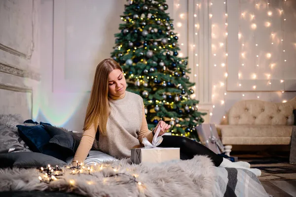 一个穿着长发的年轻女人坐在圣诞礼物前笑着 新年快乐 — 图库照片