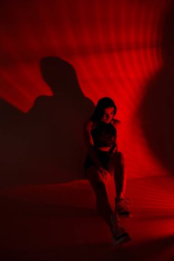 Fotoğraf stüdyosundaki genç bir esmerin fotoğrafı. Siyah bluzlu güzel, ince bir kadın ve kırmızı şortlu..