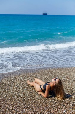 Güzel bir atletik vücudu olan ve kumlu bir plajda poz veren mayolu muhteşem bir manken. Uzun saçlı bronzlaşmış genç bir kadın dinleniyor ve güneşleniyor. Deniz kenarında büyüleyici bir model..