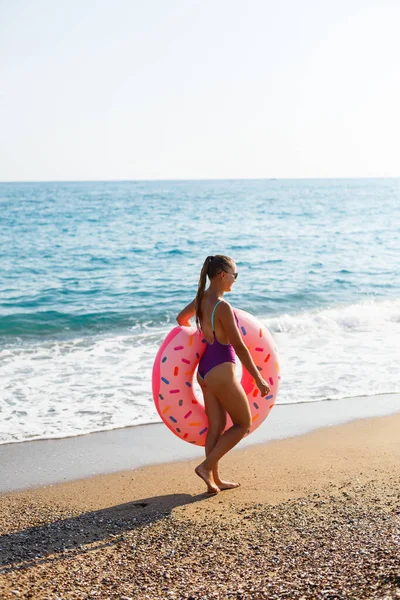 ビーチの女性は海でインフレータブルリングで歩き リラックスのために熱帯の楽園でリラックスして歩きます 夏休みの若いモデルの日光浴 — ストック写真