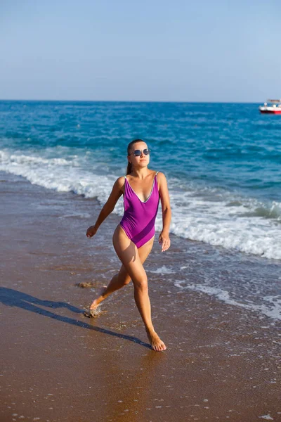 水着姿のスレンダーな女性が晴れた日に熱帯のビーチで海の波に沿って歩いています 海による夏休みのコンセプト 選択的焦点 — ストック写真
