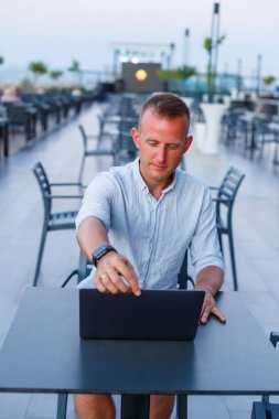 Başarılı bir erkek serbest iş adamı tatilde dizüstü bilgisayar kullanıyor. İş, ders çalışmak, serbest çalışmak. Uzak çalışma