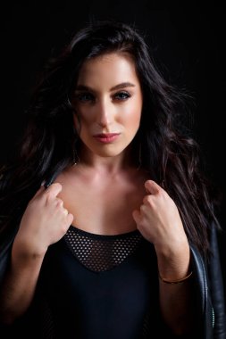 Siyah elbiseli genç bir kadın stüdyoda siyah arka planda poz veriyor.