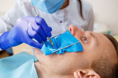 Kadın dişçi, dişçi kliniğinde enstrümanları olan hastayı muayene ediyor. Doktor dişçi koltuğundaki birinin dişlerinde diş tedavisi uygular. Seçici odak