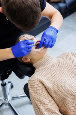 Klinikte metal diş telli bir kadının dişleri tedavi ediliyor. Bir ortodontist dişlerine diş teli takmak için diş aletleri kullanır. Seçici odak