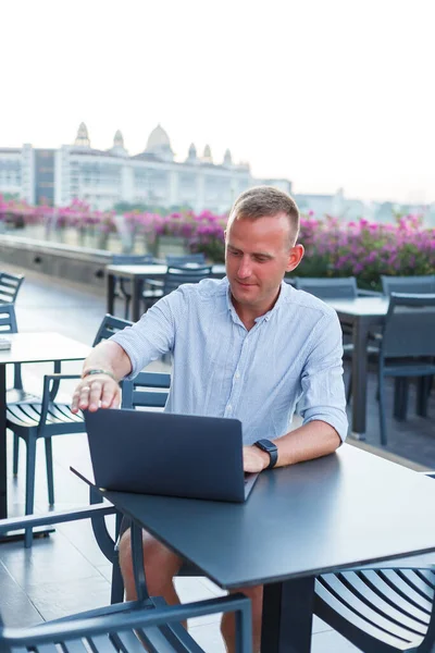 Pomyślny młody biznesmen pracujący z laptopem na wakacjach. Nosi koszulę i białe szorty. Praca poza biurem, wolny strzelec — Zdjęcie stockowe