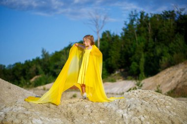 Sarı elbiseli güzel sarışın kız doğada poz veriyor. Yaz fotoğrafı. Mavi gökyüzü. Güneşli bir gün.