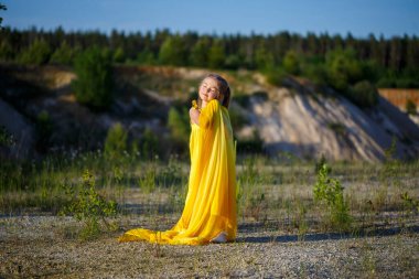 Sarı elbiseli güzel sarışın kız doğada poz veriyor. Yaz fotoğrafı. Mavi gökyüzü. Güneşli bir gün.