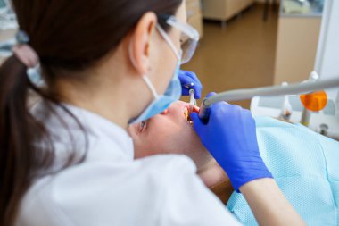 Bir hastayı tedavi ederken kadın dişçi. Doktor dişçi koltuğundaki birinin dişlerinde diş tedavisi uygular. Seçici odak.