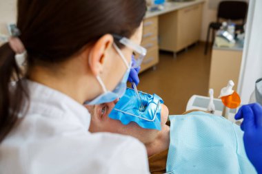 Erkek hasta dişçi koltuğuna oturur ve dişlerini yeniler, dişçi kliniğinde kadın dişçiye gider. Seçici odak