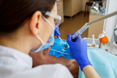 Erkek hasta dişçi koltuğuna oturur ve dişlerini yeniler, dişçi kliniğinde kadın dişçiye gider. Seçici odak