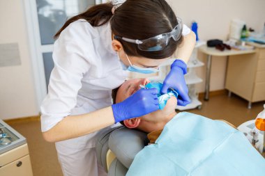 Kadın dişçi, dişçi kliniğinde enstrümanları olan hastayı muayene ediyor. Doktor, dişçi koltuğunda oturan birinin dişlerinde diş tedavisi uygular. Seçici odak