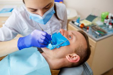 Kadın dişçi, dişçi kliniğinde enstrümanları olan hastayı muayene ediyor. Doktor, dişçi koltuğunda oturan birinin dişlerinde diş tedavisi uygular. Seçici odak