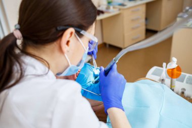 Bir dişçi, dişçi aletleriyle erkek bir hastayı tedavi eder. Diş hekimi diş kliniğindeki hastaların dişlerini muayene eder. Seçici odak