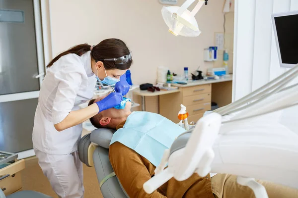 Vrouwelijke tandarts onderzoekt de patiënt met instrumenten in de tandheelkundige kliniek. De arts maakt tandheelkundige behandeling op de tanden van een persoon in de tandartsstoel. Selectieve focus — Stockfoto