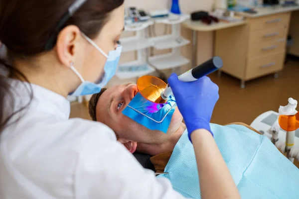 Woman dentist examines the patient with instruments in the dental clinic. The doctor makes dental treatment on the teeth of a person in the dentists chair. Selective focus — Zdjęcie stockowe