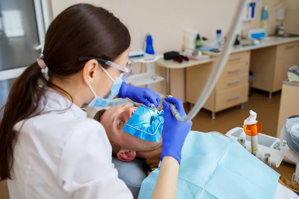A dentist treats a male patient with dental instruments. The dentist examines the teeth of the patients in the dental clinic. Selective focus — Stock Photo, Image