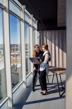 İki başarılı kadın mimar, bir dizüstü bilgisayarla pencerenin önünde dururken ortak bir projeden bahsediyorlar. İşten izin alırken resmi giyinmiş genç kadın ekonomistler konuşuyor.