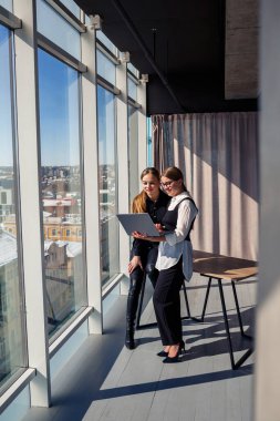 İki başarılı kadın mimar, bir dizüstü bilgisayarla pencerenin önünde dururken ortak bir projeden bahsediyorlar. İşten izin alırken resmi giyinmiş genç kadın ekonomistler konuşuyor.
