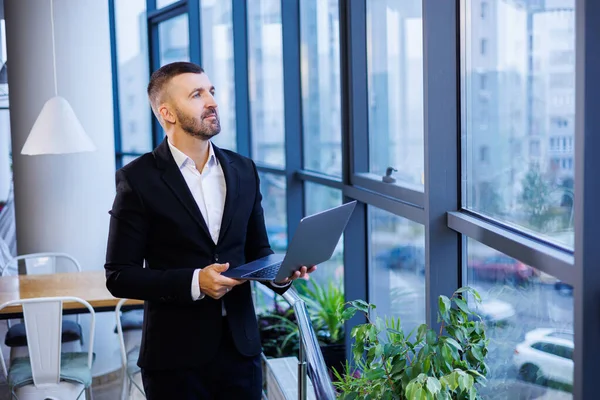 Modern ofis alanındaki büyük pencerelerin yanında oturan başarılı yakışıklı iş adamı.