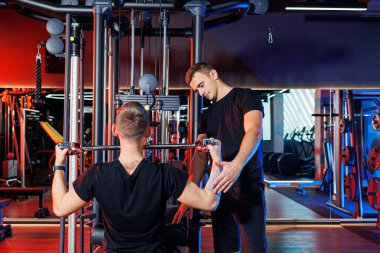 Profesyonel bir antrenörün gözetiminde spor salonunda ağır sırt egzersizleri yapan güçlü bir erkek. Sağlıklı yaşam tarzı