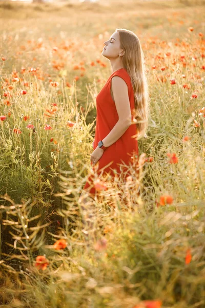 長いブロンドの髪と赤い夏のドレスを持つヨーロッパの外観の女性 彼女は咲くポピー畑に立っています — ストック写真
