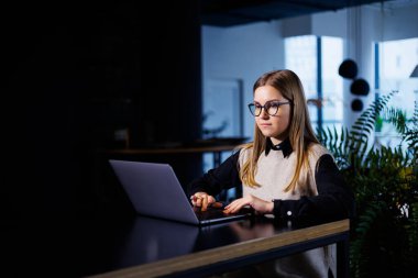 Büyük bir şirketteki güzel, çekici, zarif kadın iş kadını uluslararası iş ortaklarıyla çevrimiçi bir toplantı yapıyor. İş yerindeki bir masada dizüstü bilgisayarla oturuyor.