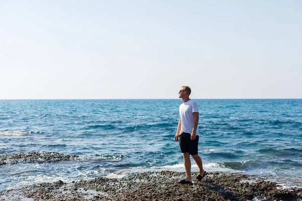 Young Attractive Man Sunglasses White Shirt Shorts Stands Shore Mediterranean — Φωτογραφία Αρχείου