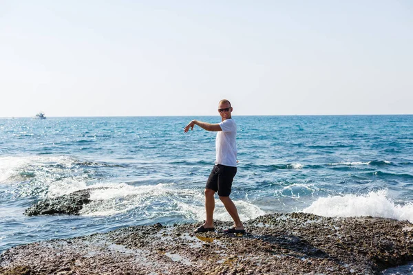 Young Attractive Man Sunglasses White Shirt Shorts Stands Shore Mediterranean — Φωτογραφία Αρχείου
