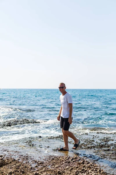 Young Attractive Man Sunglasses White Shirt Shorts Stands Shore Mediterranean — Φωτογραφία Αρχείου