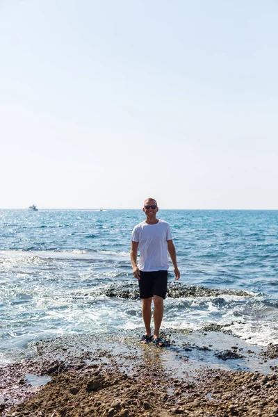 Young Attractive Man Sunglasses White Shirt Shorts Stands Shore Mediterranean — Φωτογραφία Αρχείου