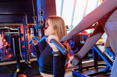 Deneyimli bir özel antrenör, son teknoloji spor salonunda kas egzersizleri sırasında atletik bir kadını denetliyor..