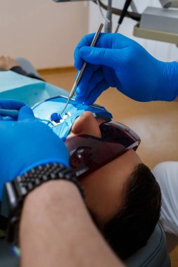 Diş hekimi diş aletini tutarken ağzı açık bir hasta dişçi koltuğunda yatıyor. Modern bir diş kliniğinde diş tedavisi. seçici odak