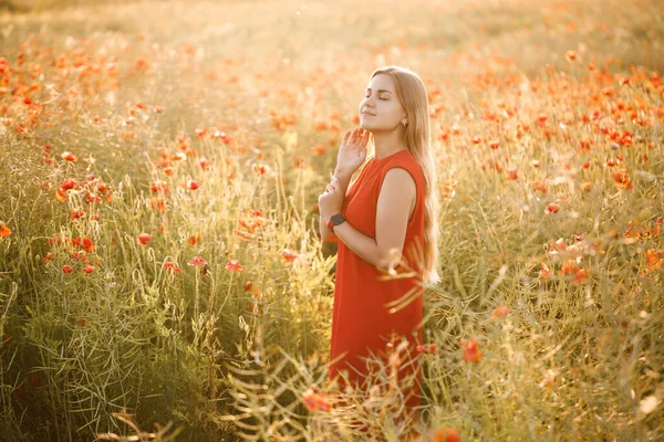 長いブロンドの髪と赤い夏のドレスを持つヨーロッパの外観の女性 彼女は咲くポピー畑に立っています — ストック写真