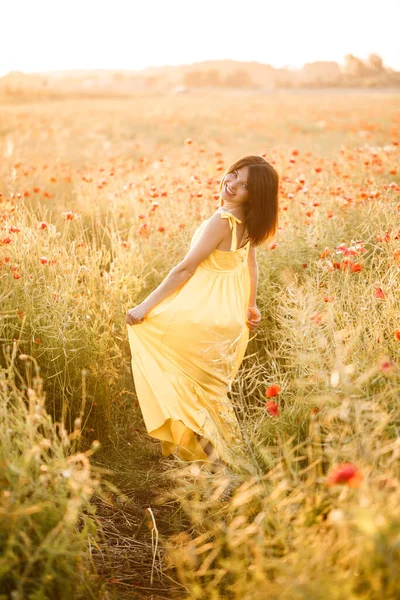 夏の日にケシ畑を歩く黄色のドレスの美しい若い女性 田舎で花を楽しむ少女 選択的焦点 — ストック写真