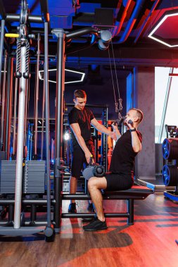 Profesyonel bir antrenörün gözetiminde spor salonunda ağır sırt egzersizleri yapan güçlü bir erkek. Sağlıklı yaşam tarzı