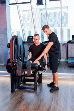 Güçlü bir genç adam spor salonunda bir antrenörün gözetiminde egzersiz yapar. Yakışıklı bir adamdan güçlü bir egzersiz. Sağlıklı yaşam tarzı