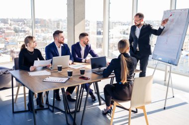 Kendine güvenen işadamı, bir şirket toplantısında yönetim kurulunda yeni bir projenin sunumunu yapıyor. Güzel denetçiler, beyaz tahta ve grafikler kullanarak farklı ortaklarla iş hakkında konuşurlar..