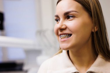 Yüzünde diş teli olan bir kadın dişçi muayenehanesinde doktorunu bekliyor. Modern bir diş kliniğinde dolap.