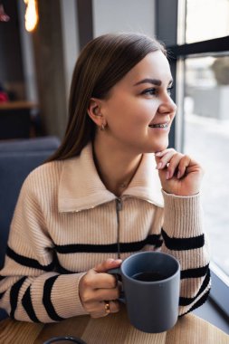 Genç, güzel bir kadın kahve içer ve pencerenin yanındaki bir kafede otururken pencereden dışarı bakar. Genç bayan sabahtan zevk alıyor. Sabah kahvesi canlandırıcı.