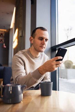 Genç bir adam bir barda cep telefonundan mesaj atıyor ve cappuccino içiyor. Genç, modaya uygun bir adam öğle yemeği sırasında bir kafede espresso içiyor ve çalışıyor.