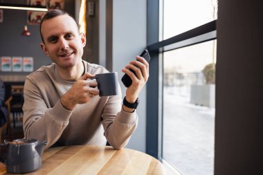 Genç bir adam bir barda cep telefonundan mesaj atıyor ve cappuccino içiyor. Genç, modaya uygun bir adam öğle yemeği sırasında bir kafede espresso içiyor ve çalışıyor.