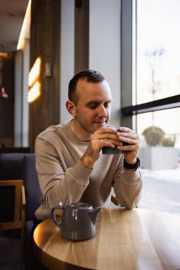 Çekici, yalnız bir adam bir kafe masasında oturur ve güzel kokulu sıcak çay içer. Günlük kıyafetlerle gülümseyen adam bir kafede oturur ve kahve içer.